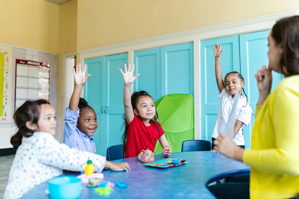 Students sit at a classroom table with their teacher