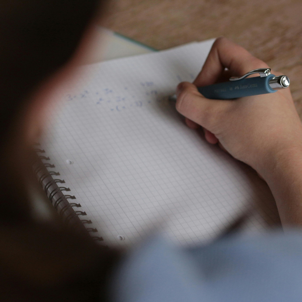 A person does math problems using a pen in a paper workbook.